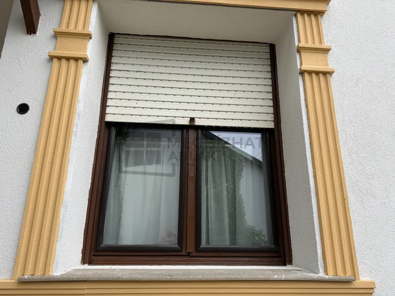 Régi, részben leengedett műanyag redőny egy faablak előtt