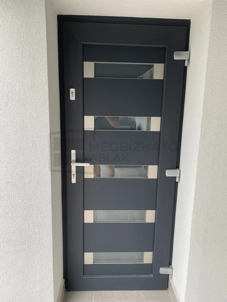 Kifelé nyíló Decco 82 műanyag bejárati ajtó Aldrin Premium panellel, savmart üveggel és felső másodzárral; kívül Coal Grey Sand antracit, belül fehér kivitelben