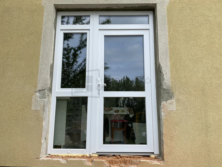 Fehér üveges műanyag bejárati ajtó bal oldali fix oldalvilágítóval, amelynek felső részében bukóablak található